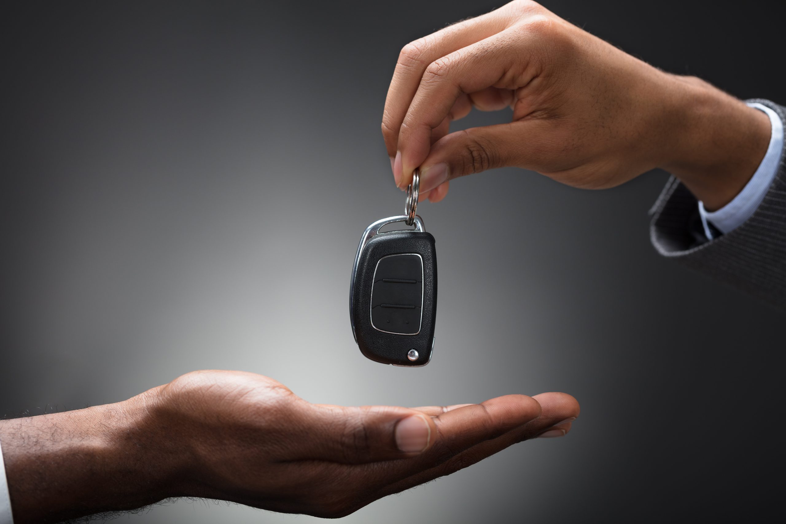 Close-up Of Hand Handing Car Key To The Person Against Gray Background